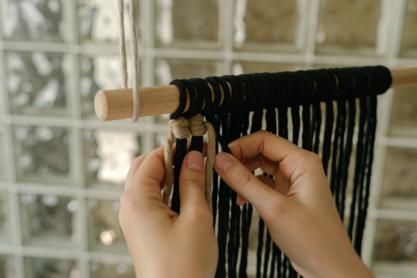 Hands knotting macramé on a vertical loom